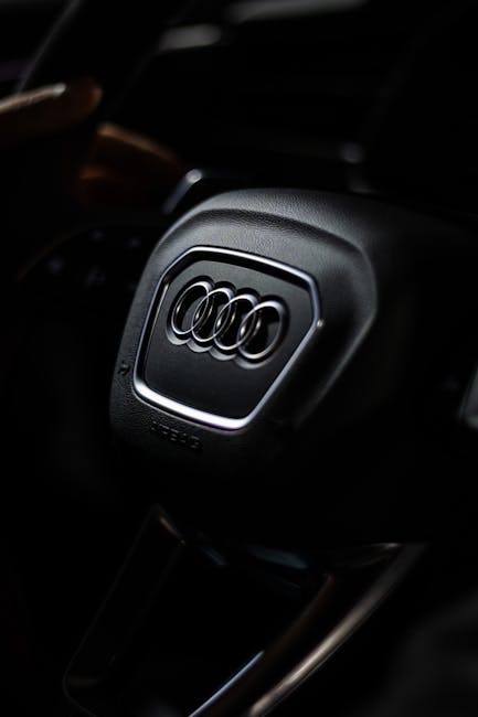 Detailed view of an Audi steering wheel highlighting brand logo with moody lighting.